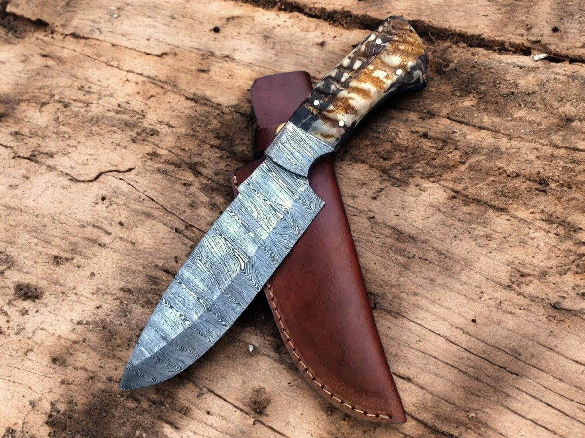 Fixed-blade knife with a patterned blade and mottled handle resting across a brown leather sheath