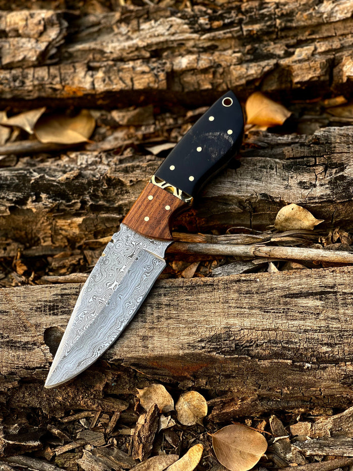 Fixed-blade hunting and skinning knife with patterned steel blade, natural horn and wood handle, and leather sheath