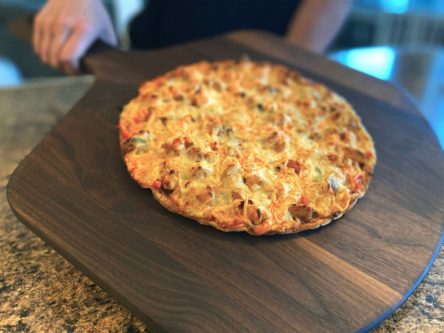 Baked pizza being carried on a wooden pizza peel