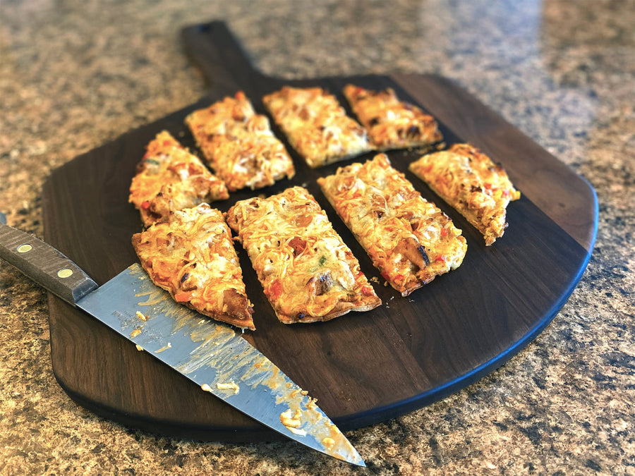 Sliced flatbread served on a walnut pizza peel beside a knife