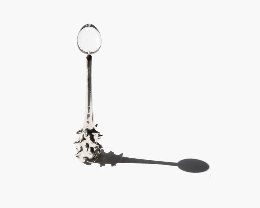 Silver Oracle candle snuffer casting a long oval shadow