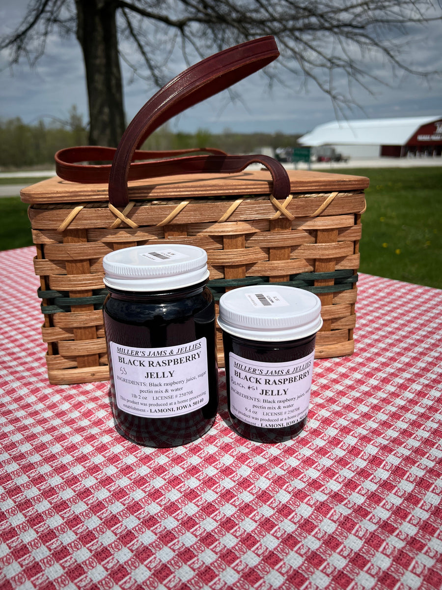 Two sizes of Miller’s Black Raspberry Jelly beside a picnic basket; jars sold separately.
