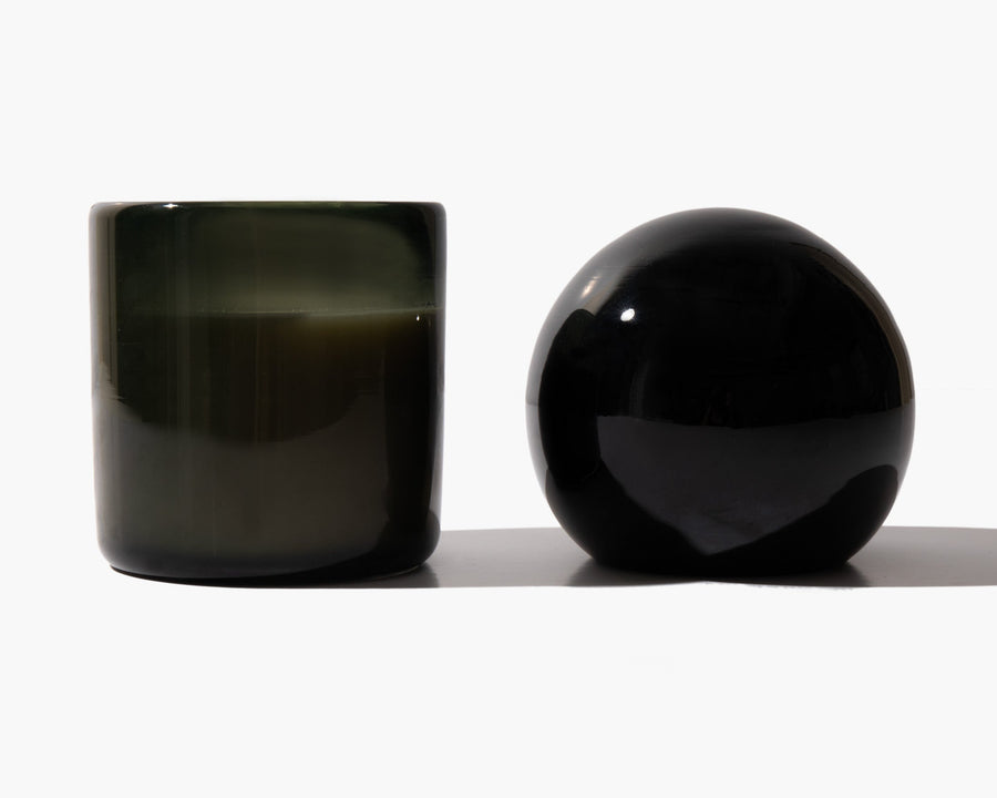 Open dark glass candle vessel beside the spherical lid