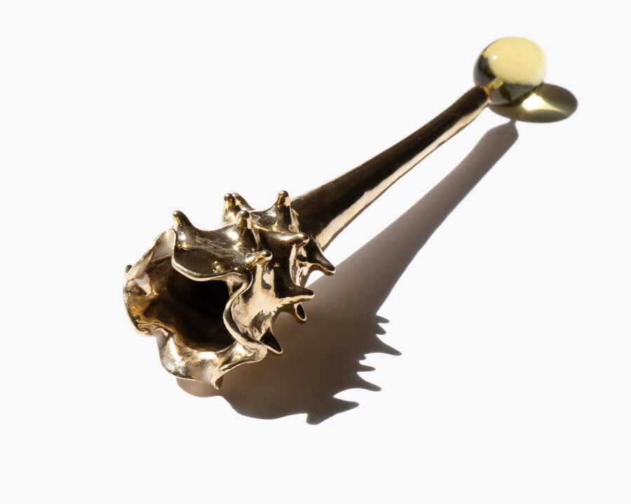 Brass Oracle snuffer lying diagonally with its textured base visible