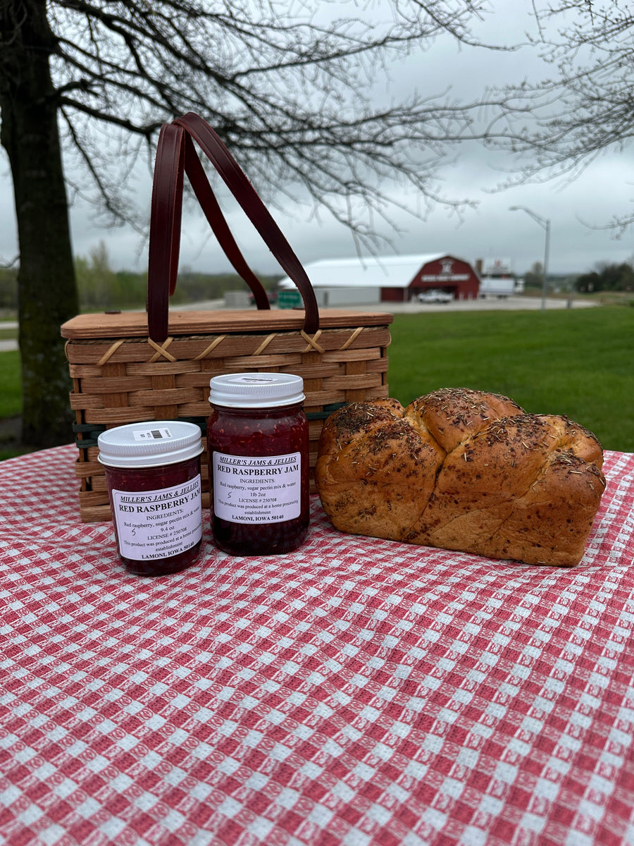 Two sizes of Miller’s Red Raspberry Jam beside bread and a picnic basket; jars sold separately.