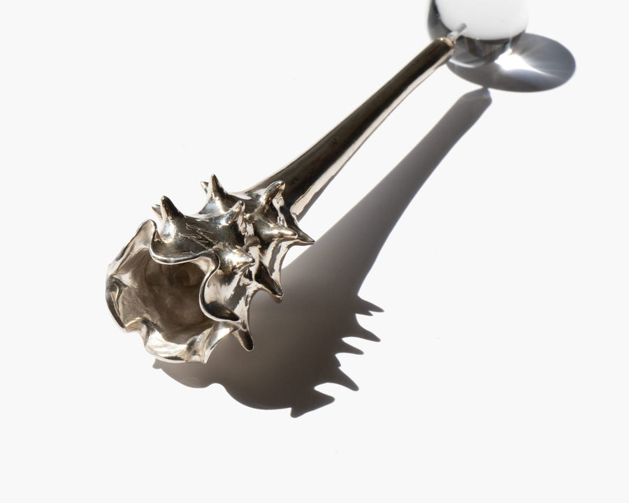 Silver Oracle snuffer lying diagonally with the base opening visible