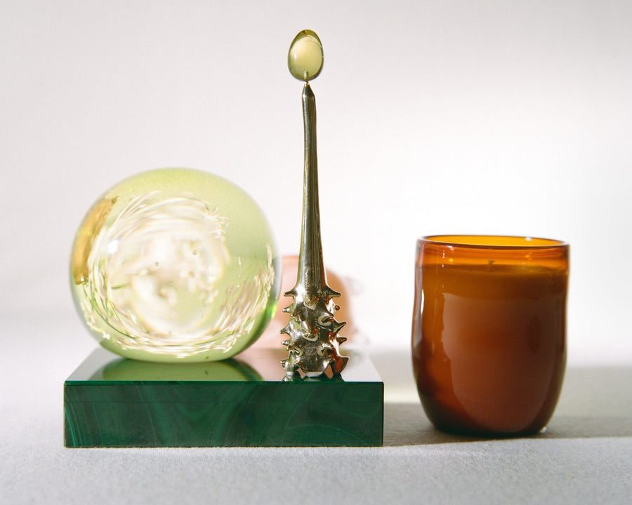 Brass Oracle snuffer beside a glass sphere and amber candle