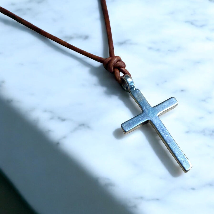 Classic cross on brown leather cord against pale stone