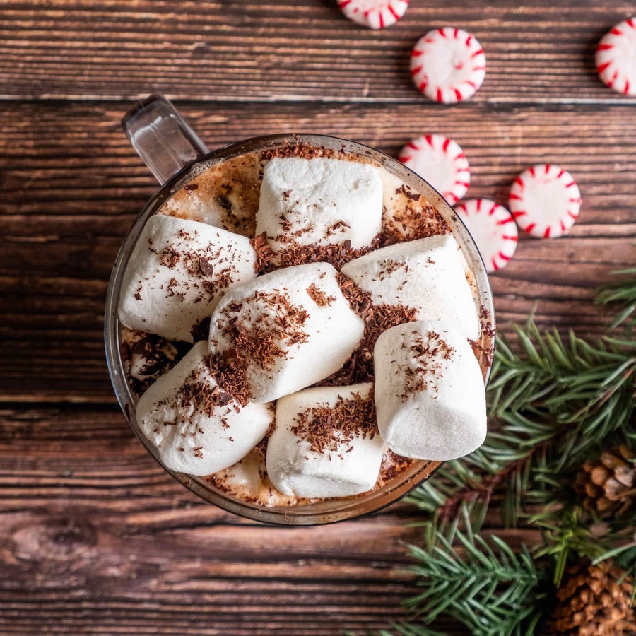 Peppermint hot cocoa topped with marshmallows beside peppermint candies