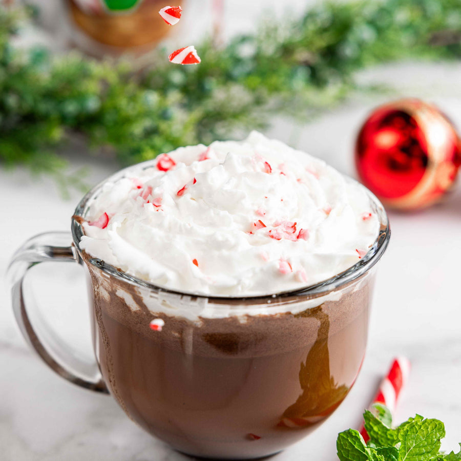 Peppermint hot chocolate in a glass cup with whipped topping and crushed candy cane