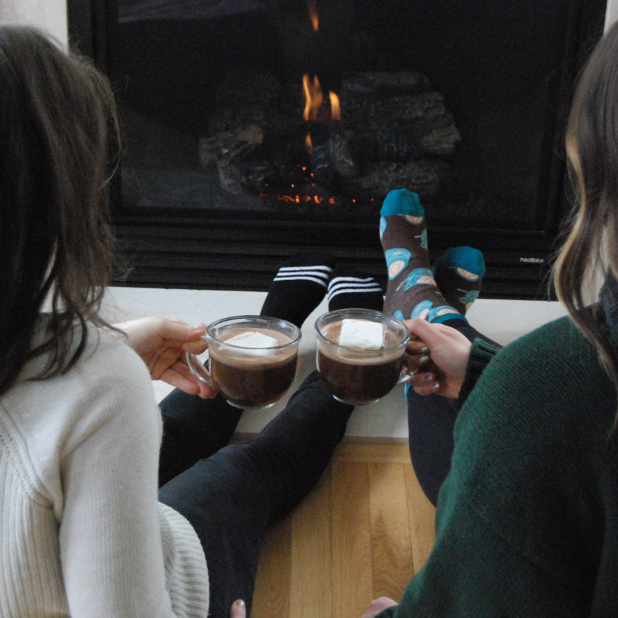 Two people holding mugs of hot cocoa beside a fireplace