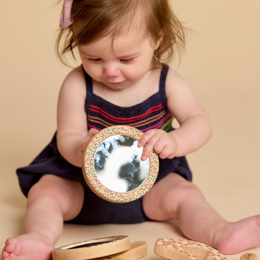Child holding a round wooden-framed discovery mirror