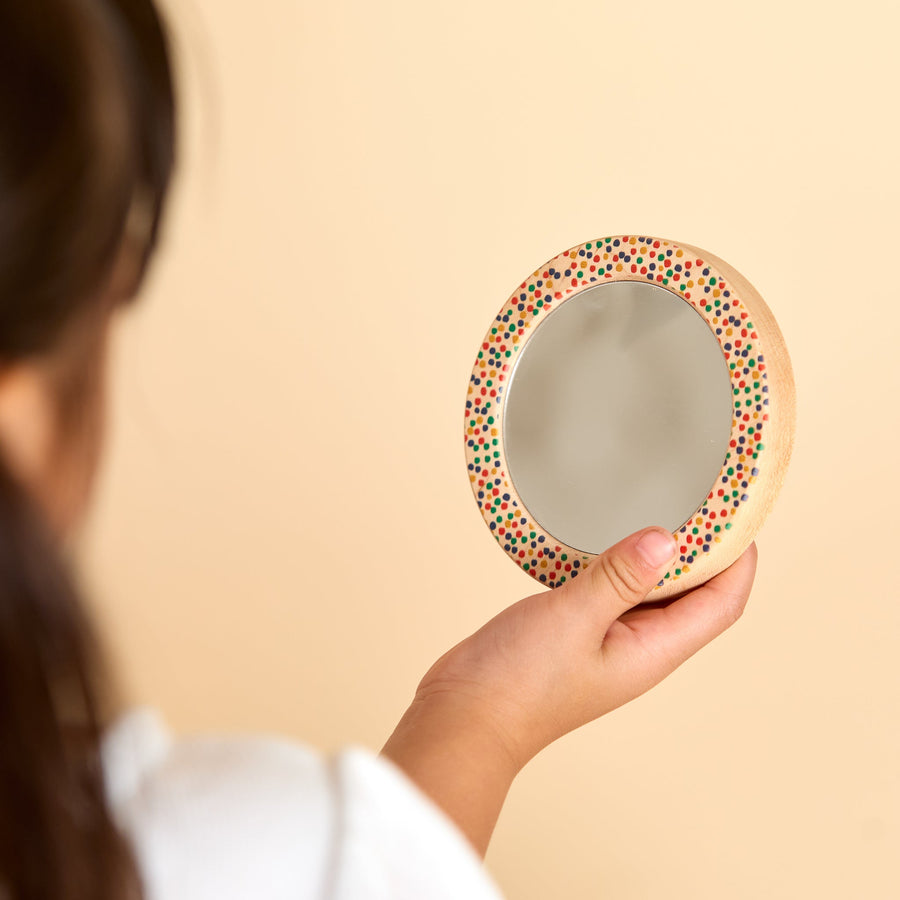 Child holding a round wooden-framed discovery mirror