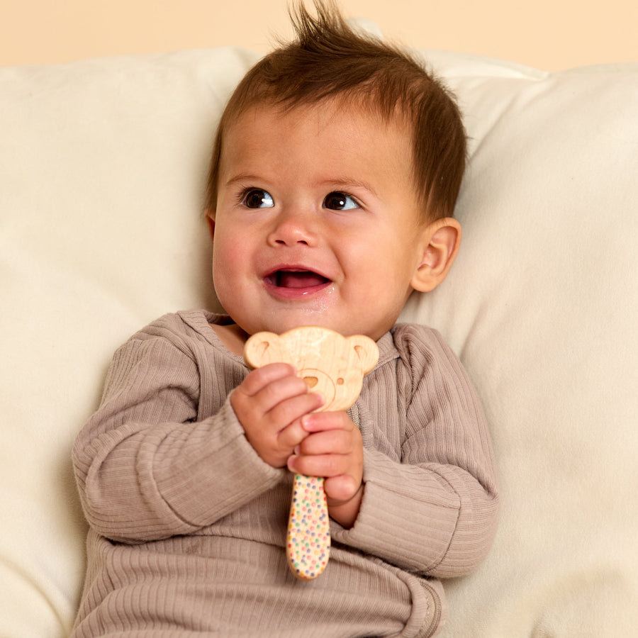Baby holding a wooden animal-shaped rattle during supervised play