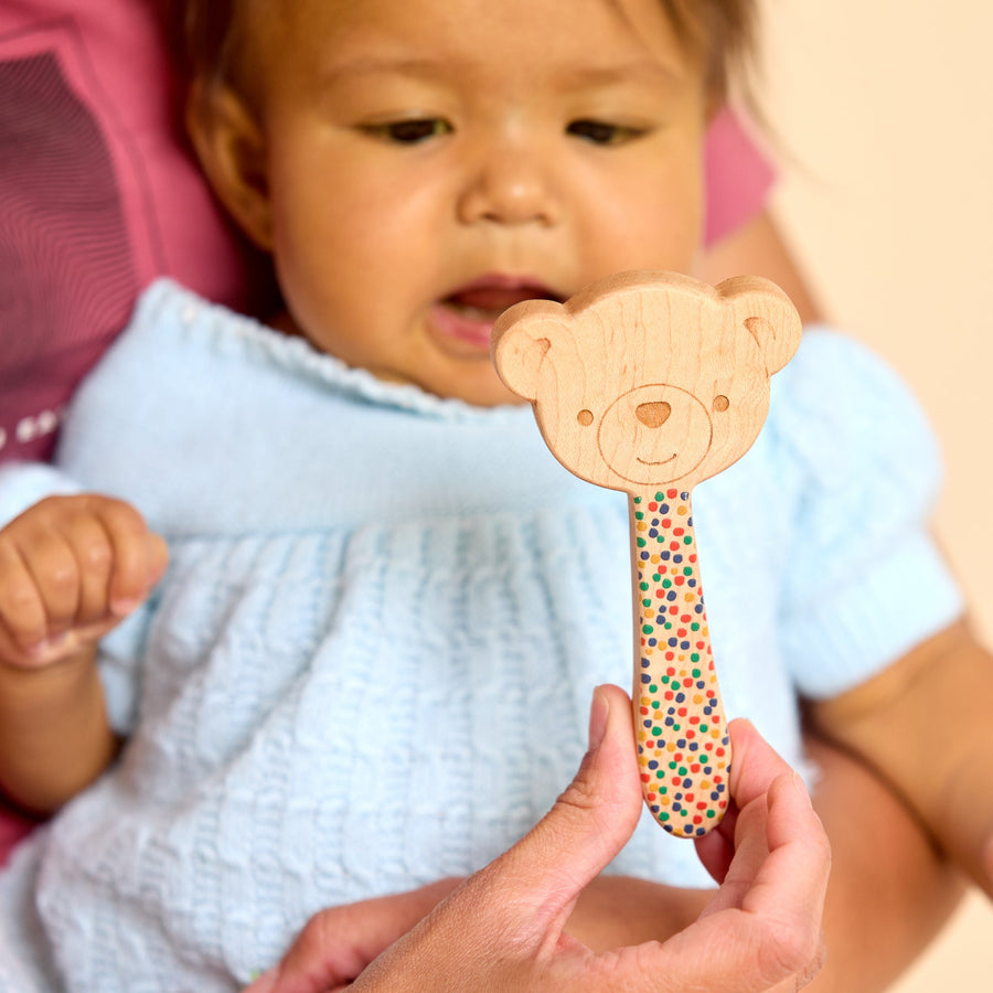 Baby holding a wooden animal-shaped rattle during supervised play