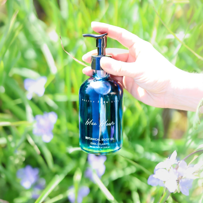 Hand holding Blue Bloom body oil among green leaves