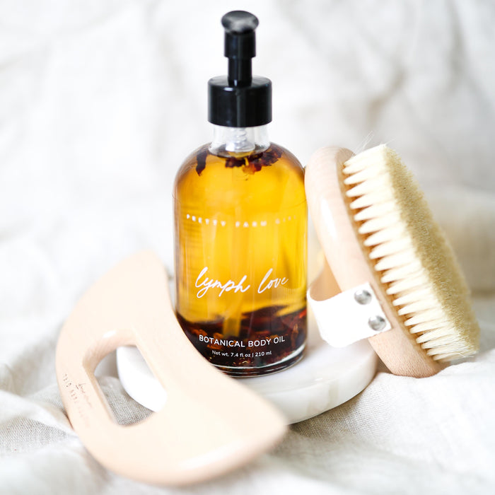 Body oil, dry brush and gua sha tool on a white surface