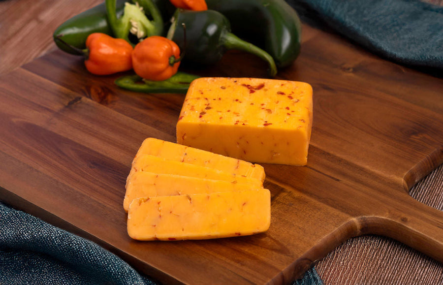 Buffalo Cheddar block on a board beside peppers