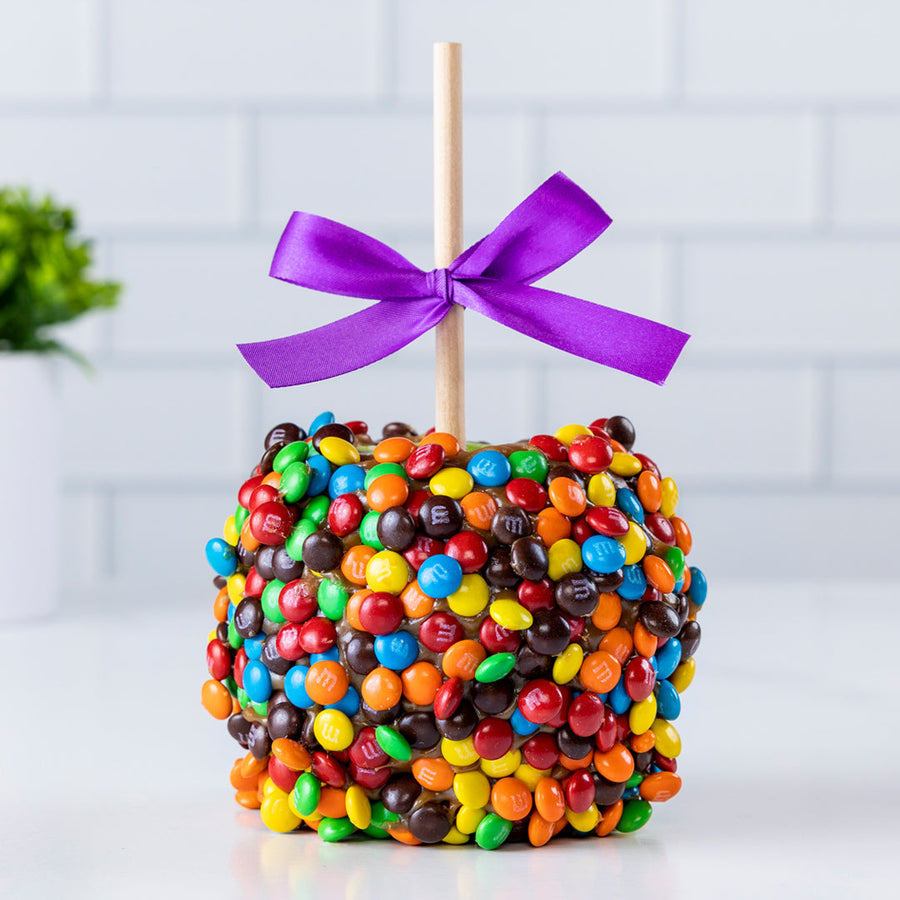 Caramel apple covered in colorful M&M candies with a purple bow
