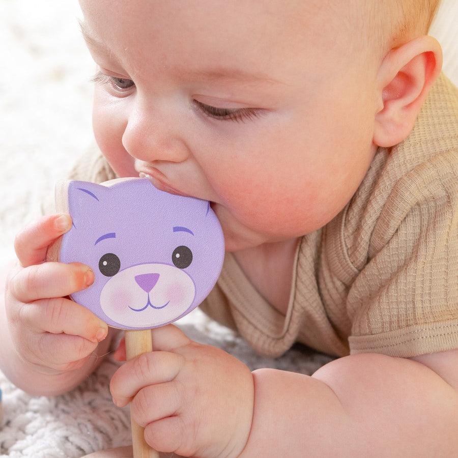 Baby holding a purple cat-shaped wooden rattle