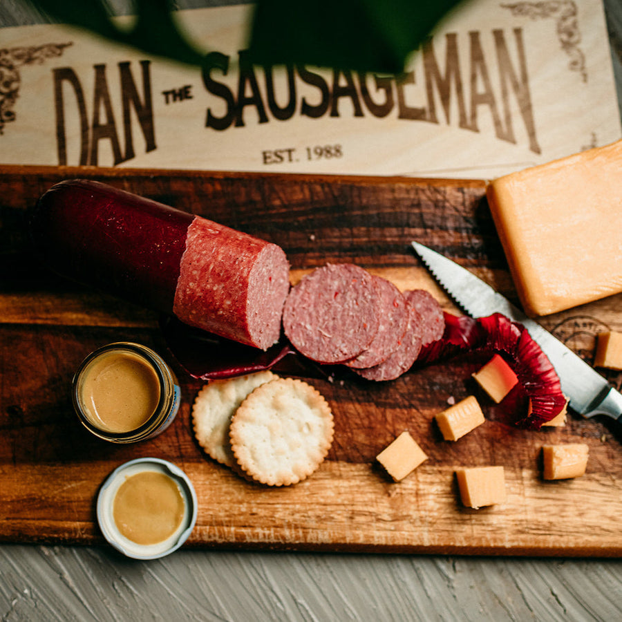Sliced sausage, cheese, crackers and mustard beside branded gift packaging