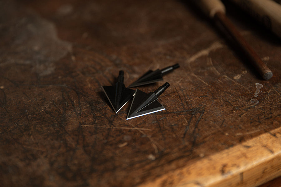 Two double-bevel broadheads on a wooden workbench