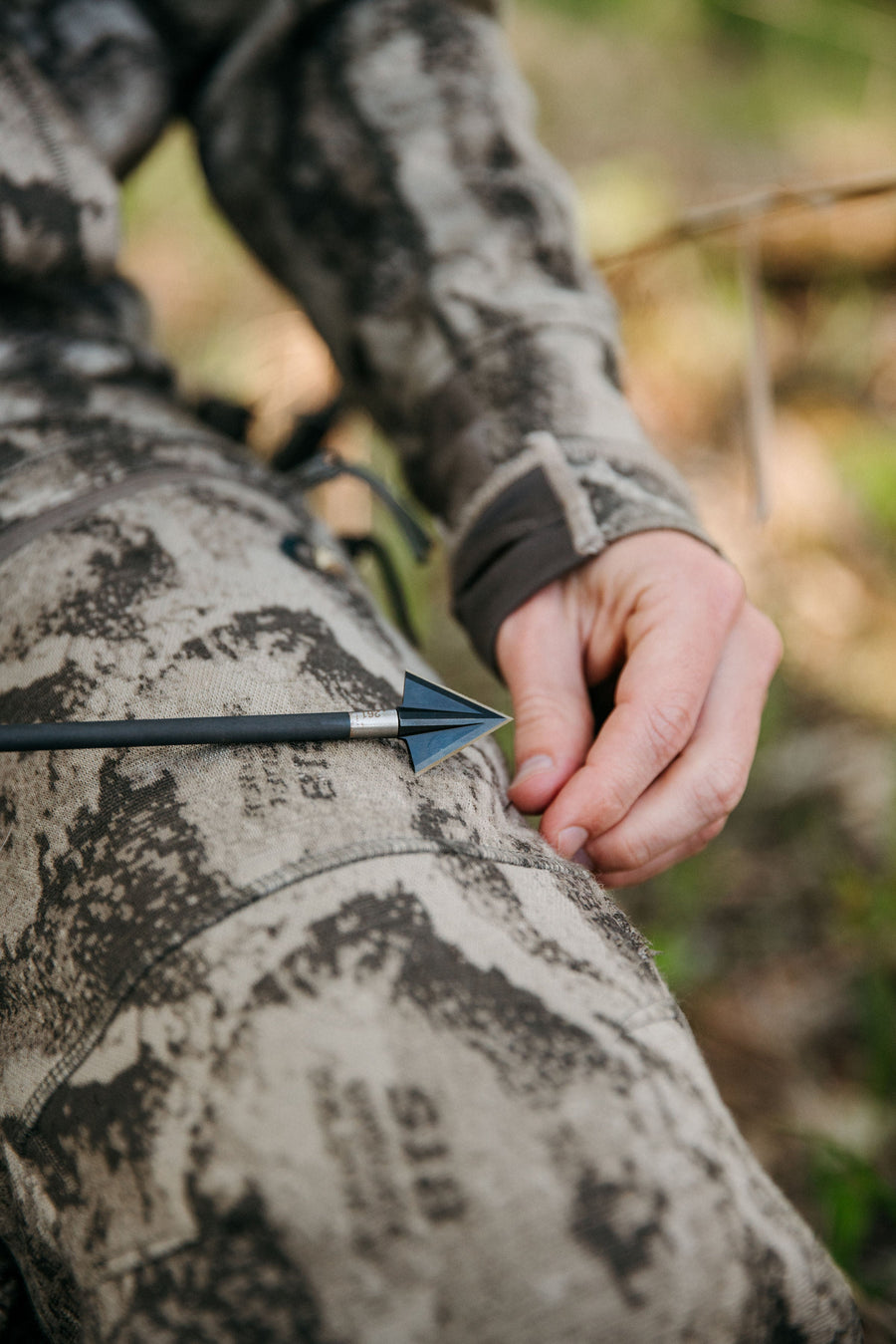 Broadhead mounted on an arrow beside camouflage clothing