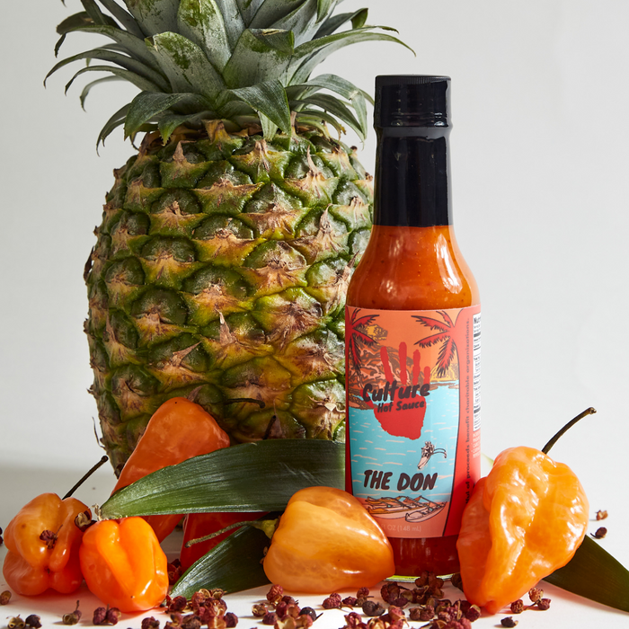 The Don hot sauce bottle beside pineapple and orange habanero peppers