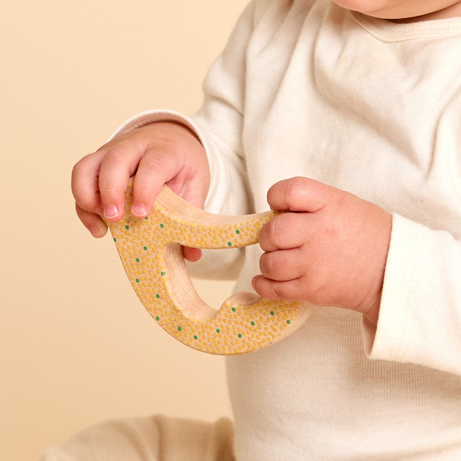 Child grasping and exploring a bird-shaped wooden rattle