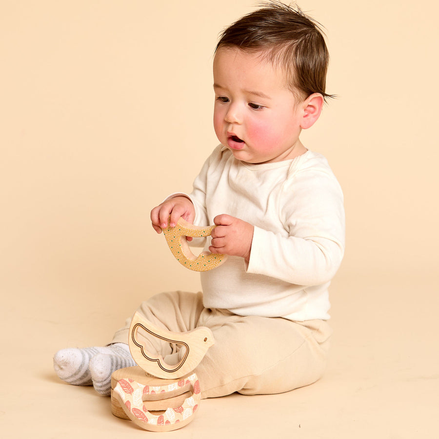 Baby holding a bird-shaped wooden rattle and teether