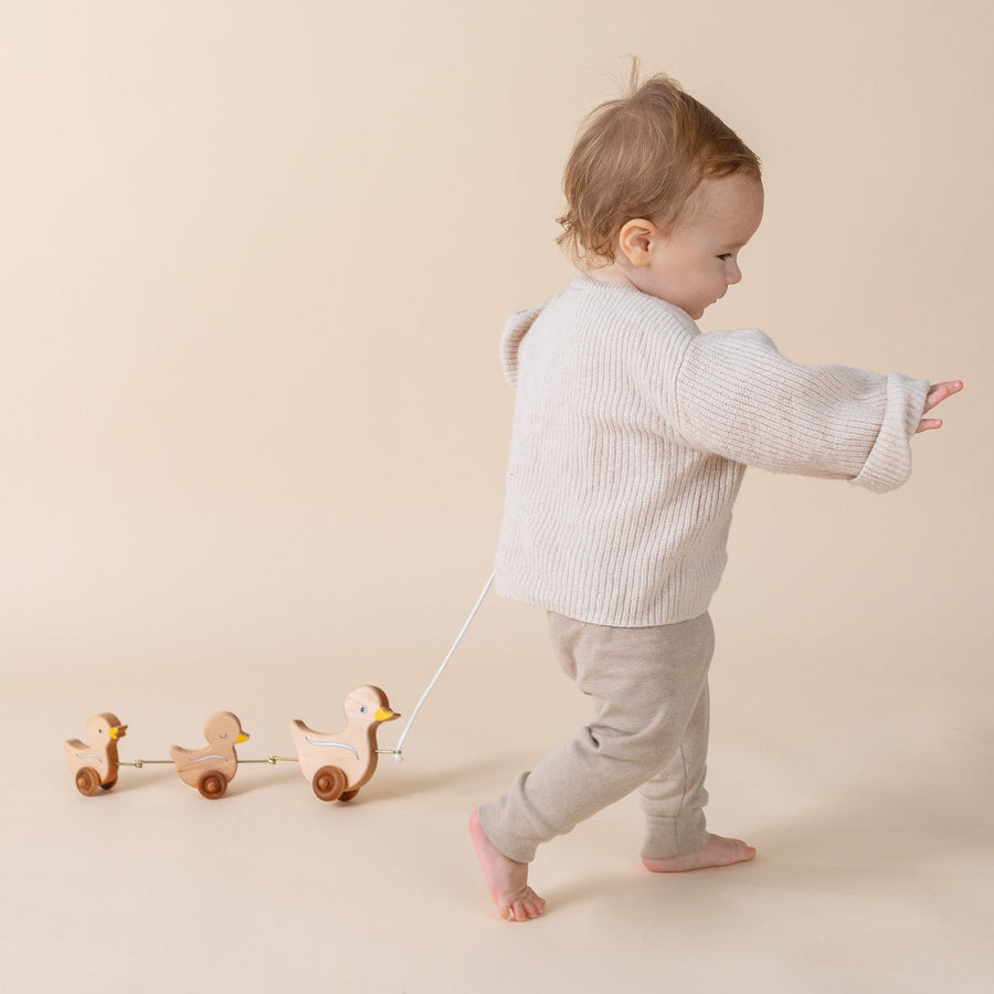Child pulling a linked wooden animal toy across the floor