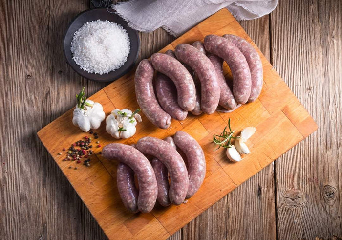 Uncooked sausage links on a cutting board with garlic and salt