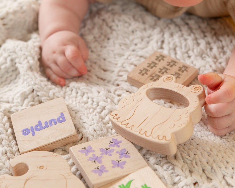 Wooden baby teethers and cotton storage bags arranged on a soft blanket