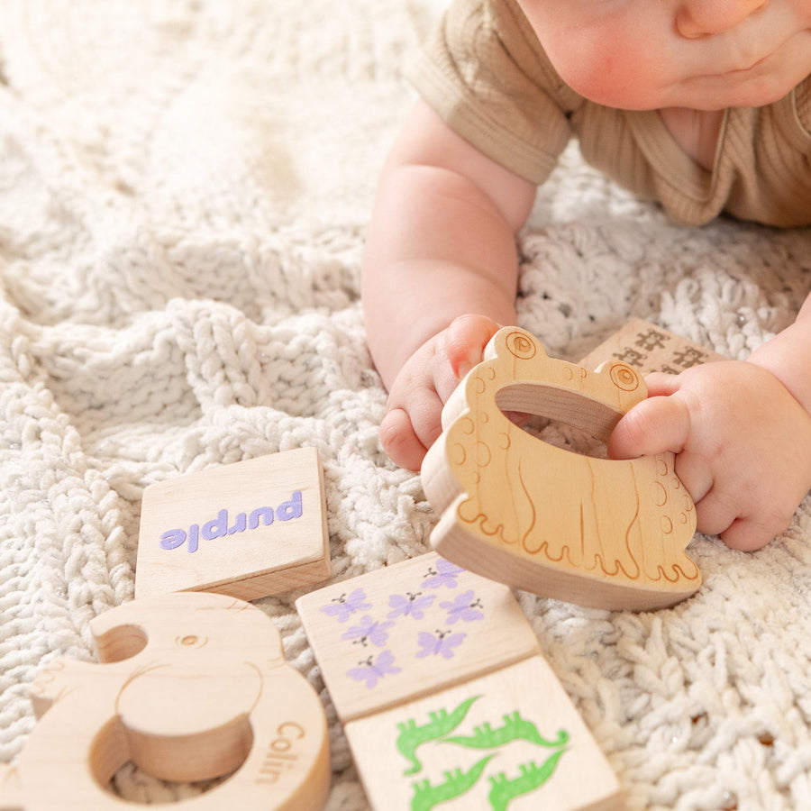 Wooden baby teethers and cotton storage bags arranged on a soft blanket