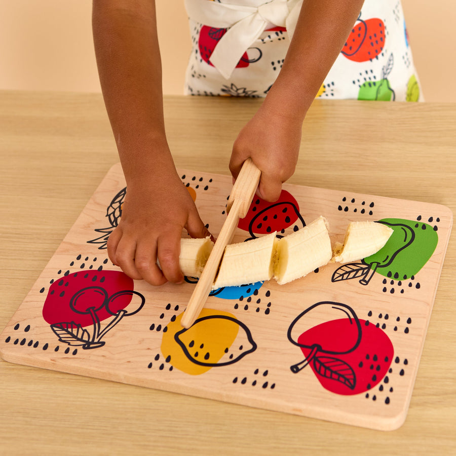 Child using a wooden knife and illustrated cutting board during food preparation