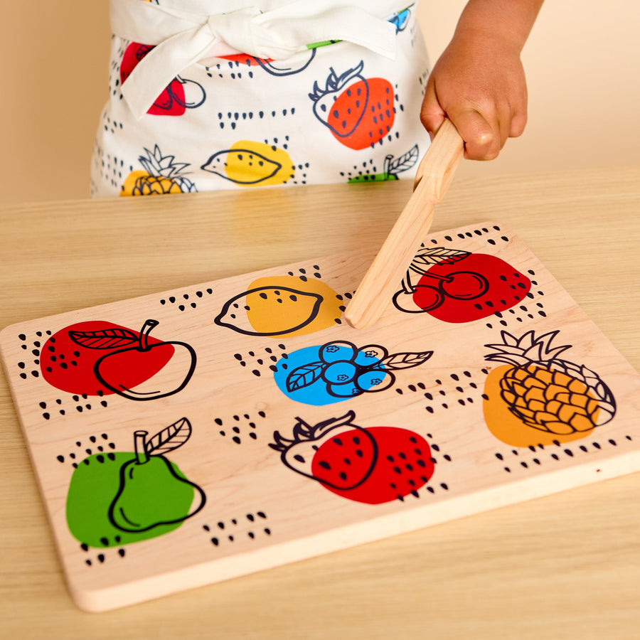Child using a wooden knife and illustrated cutting board during food preparation