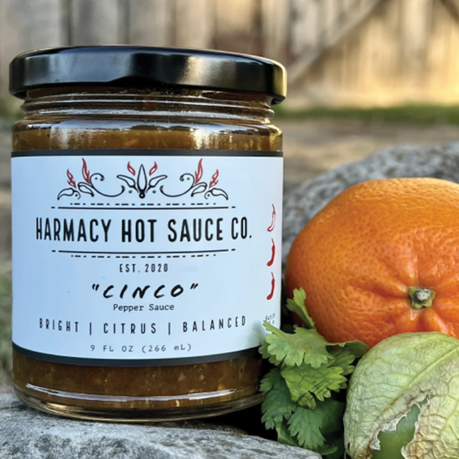 Cinco hot sauce jar beside citrus and tomatillo outdoors