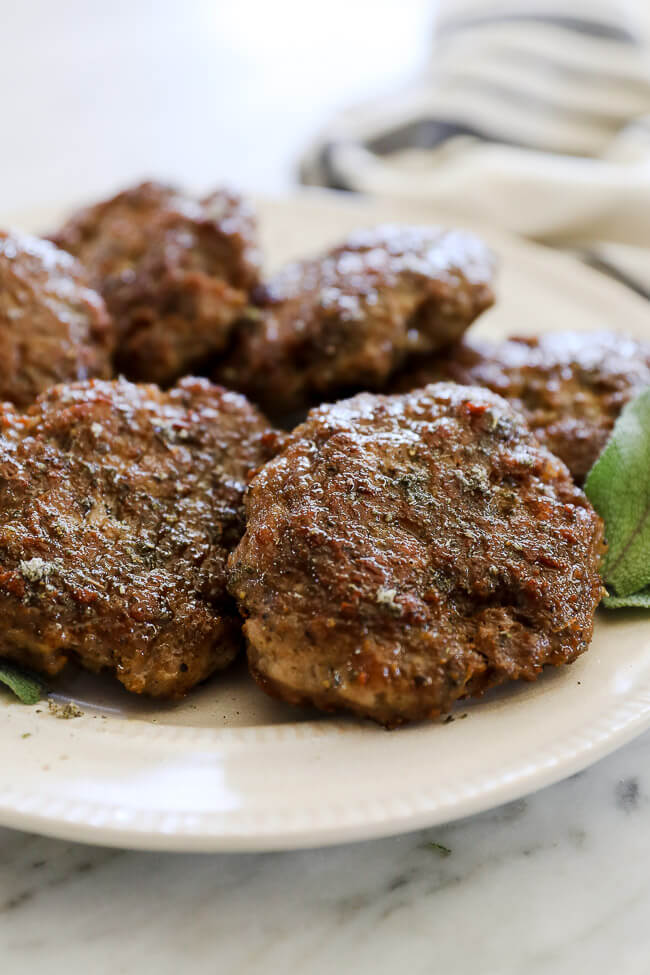 Cooked breakfast sausage patties on a white plate with a fork