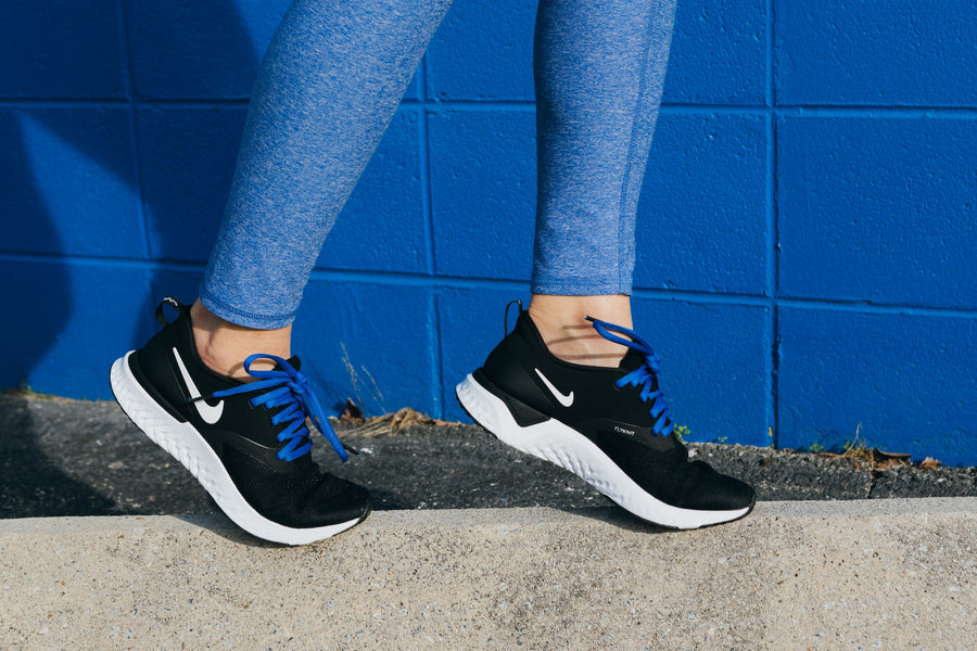 Blue oval athletic shoelaces worn with black running shoes beside a blue wall