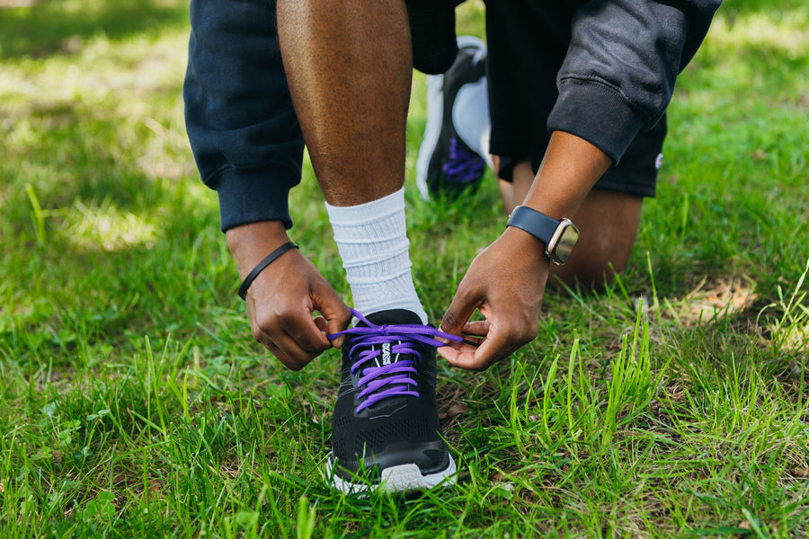 Purple oval athletic shoelaces being tied on running shoes outdoors