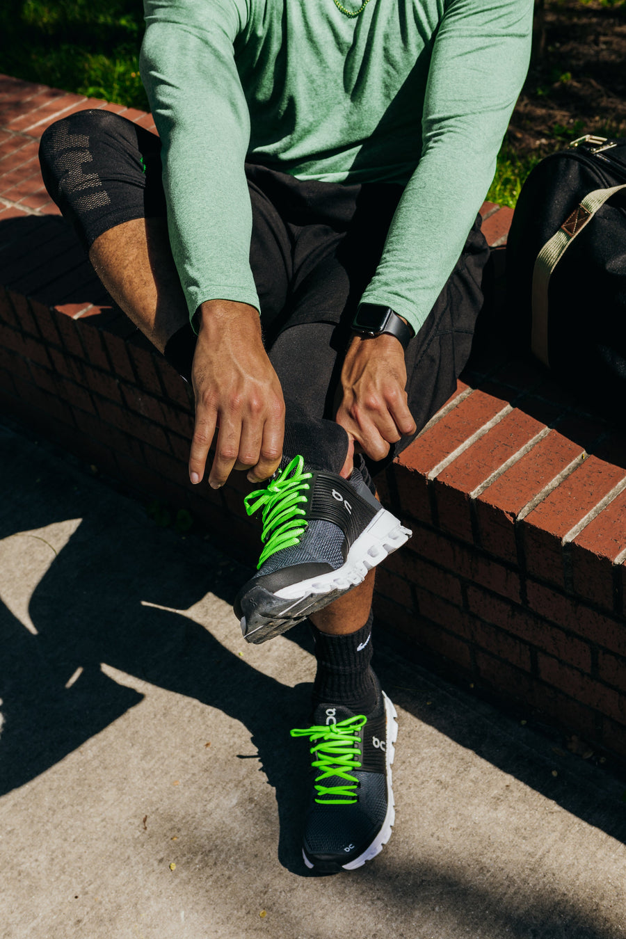 Neon Green oval athletic shoelaces being tied on dark running shoes outdoors