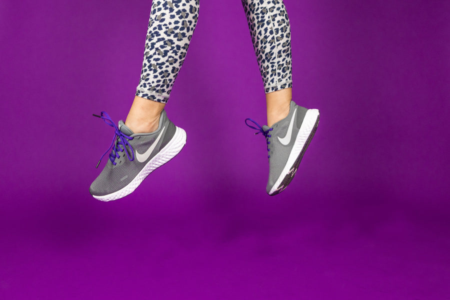 Purple oval athletic shoelaces worn with running shoes beside a purple wall