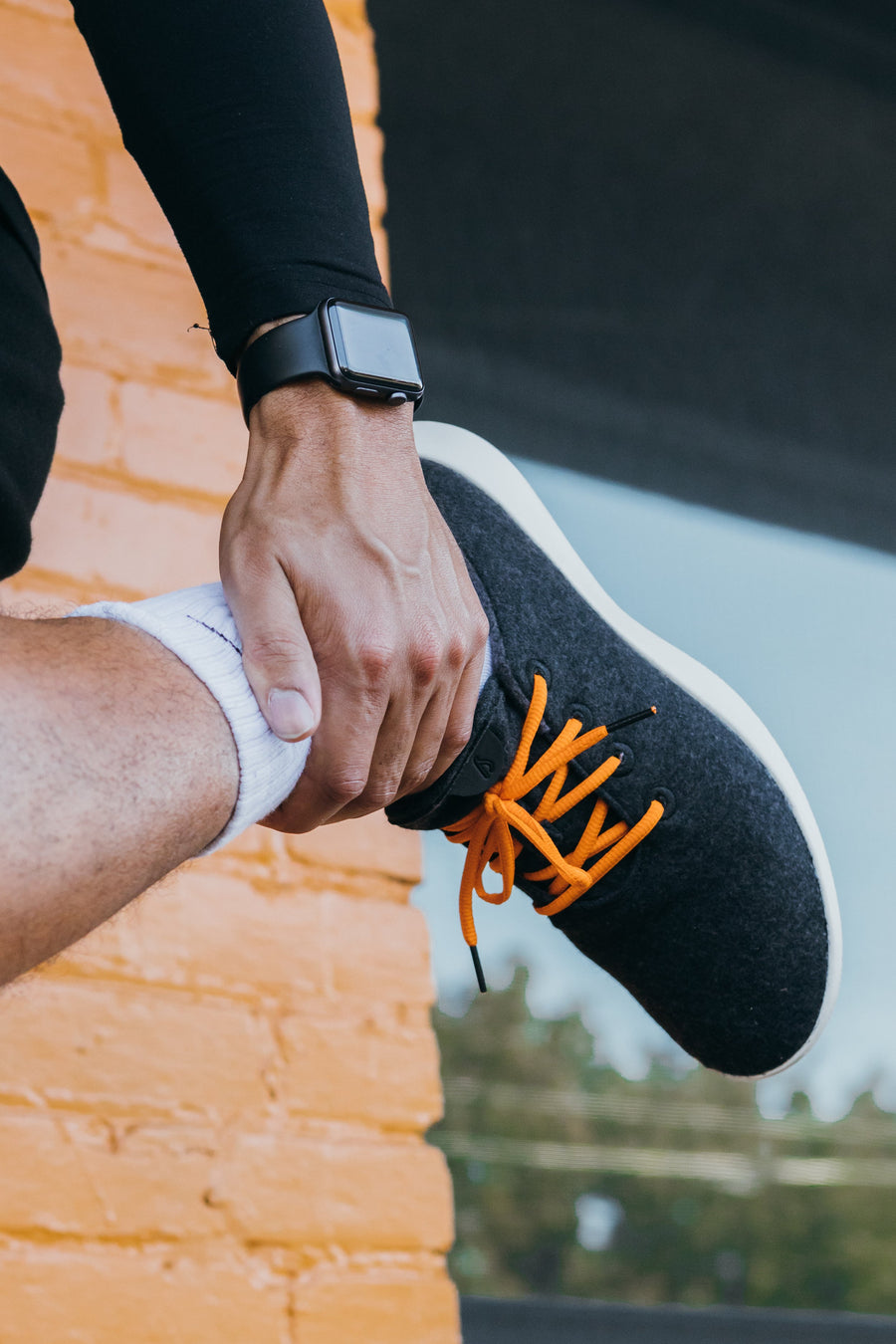 Orange oval athletic shoelaces being tied on a dark athletic shoe