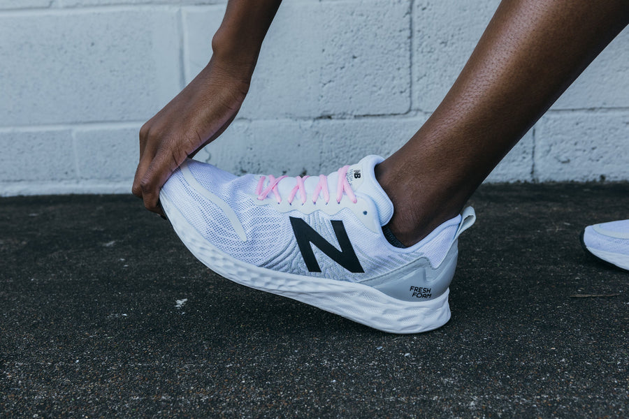 Pink oval athletic shoelaces being tied on a white athletic shoe