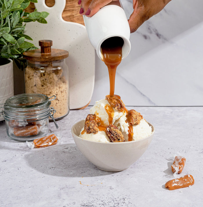 Salted Caramel candied pecans served over ice cream as caramel sauce is poured from a pitcher