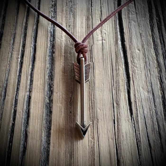Arrow pendant on brown leather cord against weathered wood