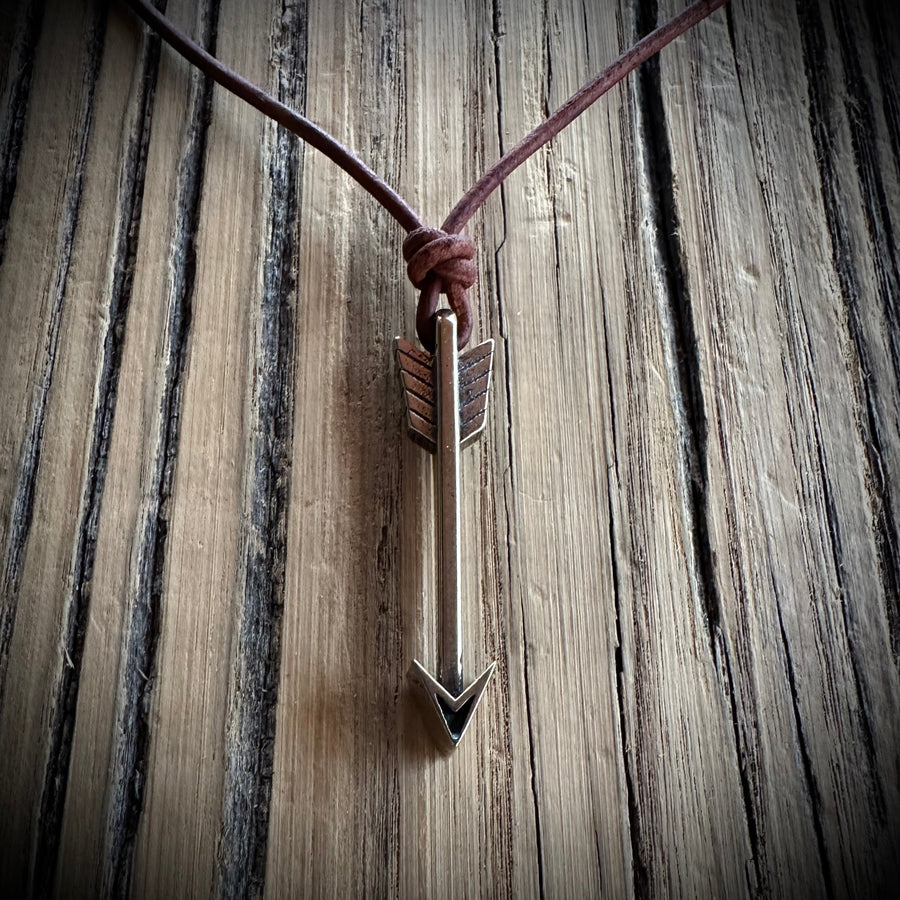 Arrow pendant on brown leather cord against weathered wood