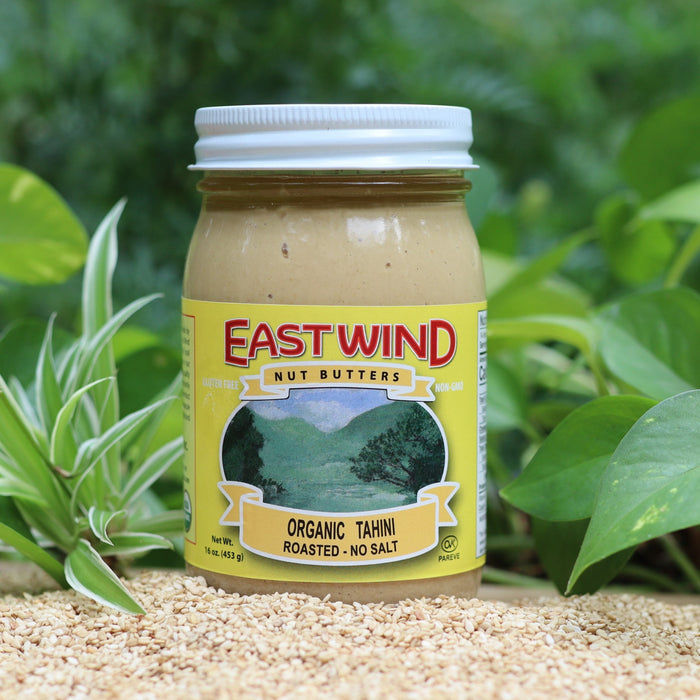East Wind organic tahini jar on a table with sesame seeds and green foliage