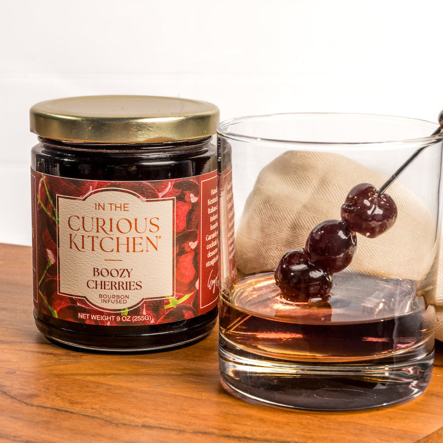 Boozy Cherries jar beside a cocktail glass and cherry garnish