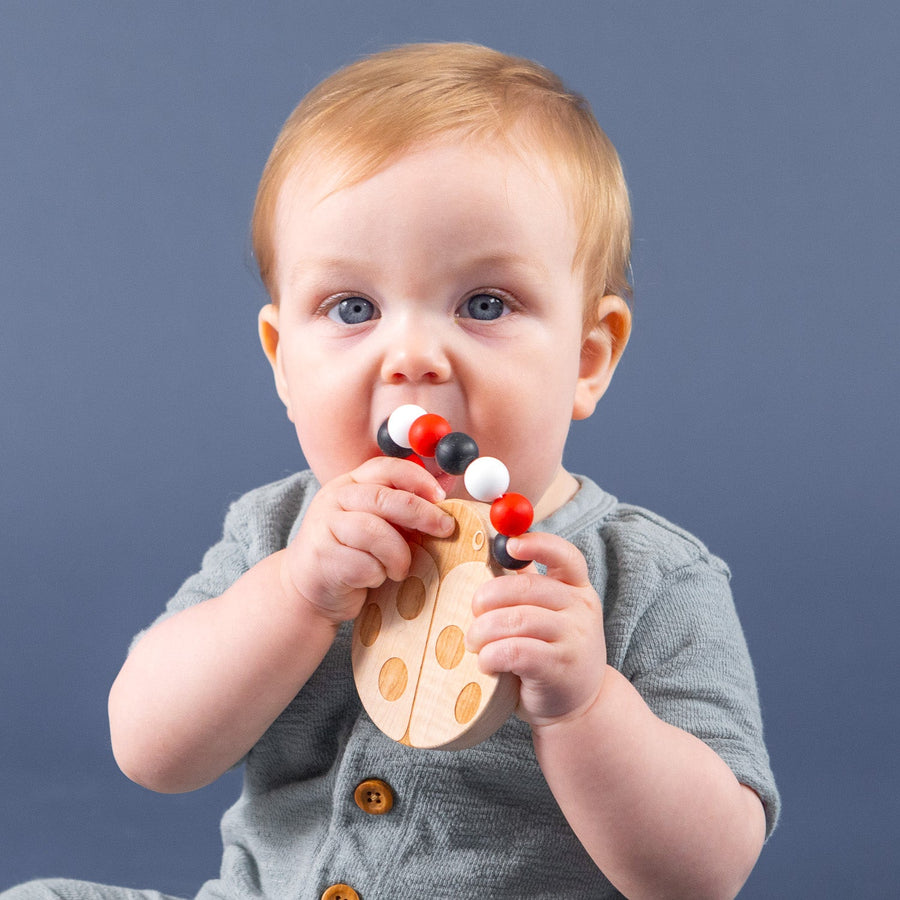 Baby holding a wooden teether with silicone beads during supervised play